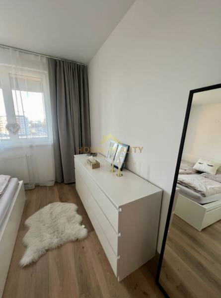 Bedroom in a 2-room apartment with wood-patterned flooring, a white dresser, and a mirror.