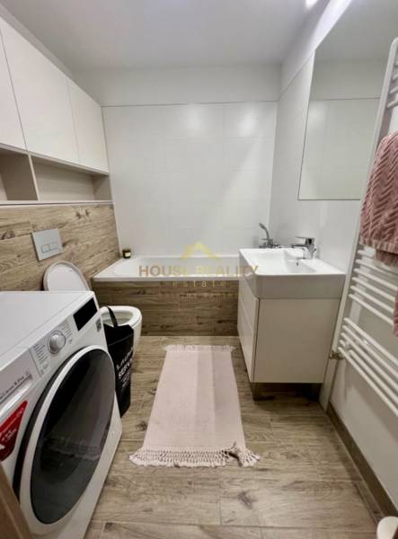 Bathroom in a 2-room apartment with a bathtub, washing machine, and floor with wood decor.