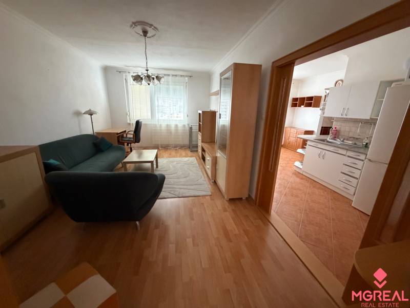 Living room in a three-room apartment with a wooden decor floor, connected to the kitchen.