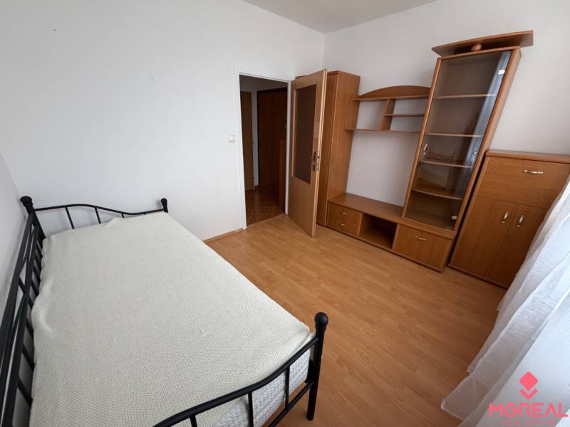 Single bed, wardrobe, and shelving unit in a 3-room apartment with a wooden decor floor.