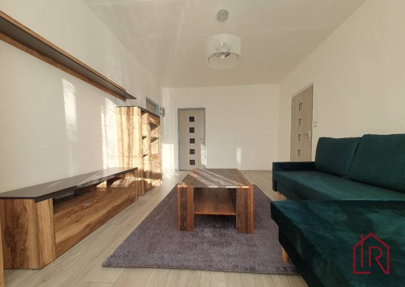 Living room in a three-room apartment with a sofa, wardrobe, and table on a wooden decor floor.