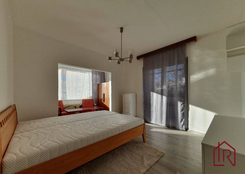 Bedroom in a 3-room apartment with a bed and a large window, wooden decor flooring.