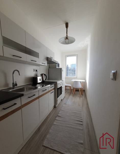 A kitchen in a 3-room apartment with a wooden decor floor and white furniture.