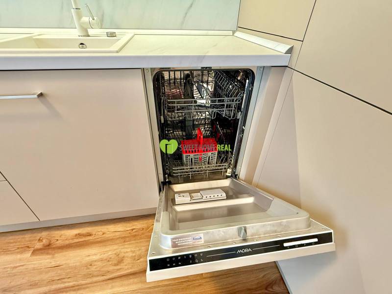 A kitchen in a 2-room apartment with a dishwasher and a wooden decor floor.