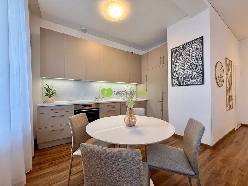 A kitchen in a 2-room apartment with light furniture and a wooden decor floor.