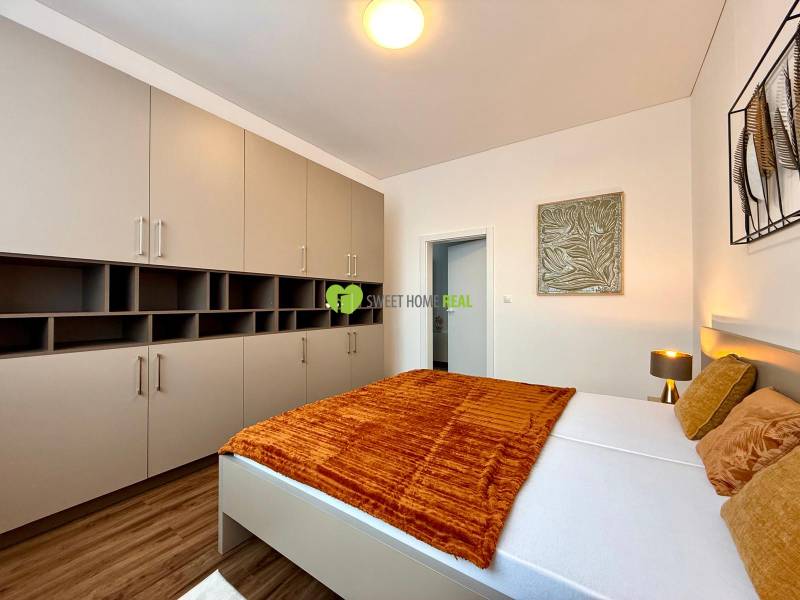 Bedroom in a two-room apartment, with wood-decor flooring and a large wardrobe.