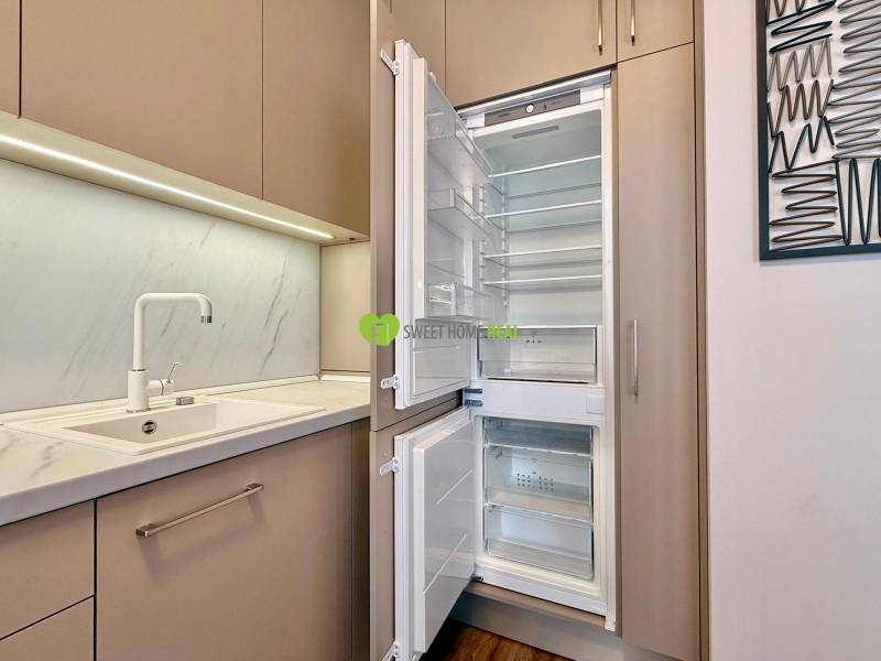 Kitchen in a 2-room apartment with a white sink and an open refrigerator.