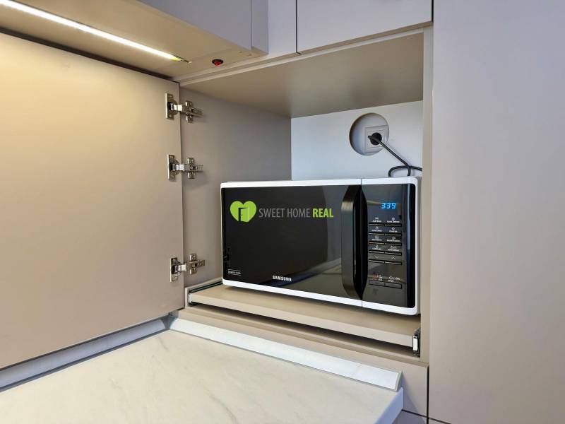 A microwave in a kitchen cabinet with a wooden floor in a 2-room apartment.