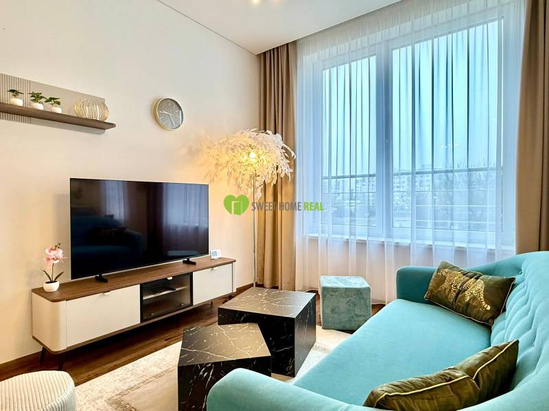 Living room in a two-room apartment with a wooden decor floor, a comfortable sofa, and a television.