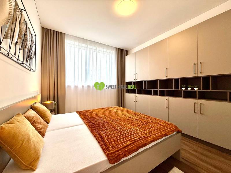 Bedroom in a 2-room apartment with wood-decor flooring, a large wardrobe, and an orange blanket.