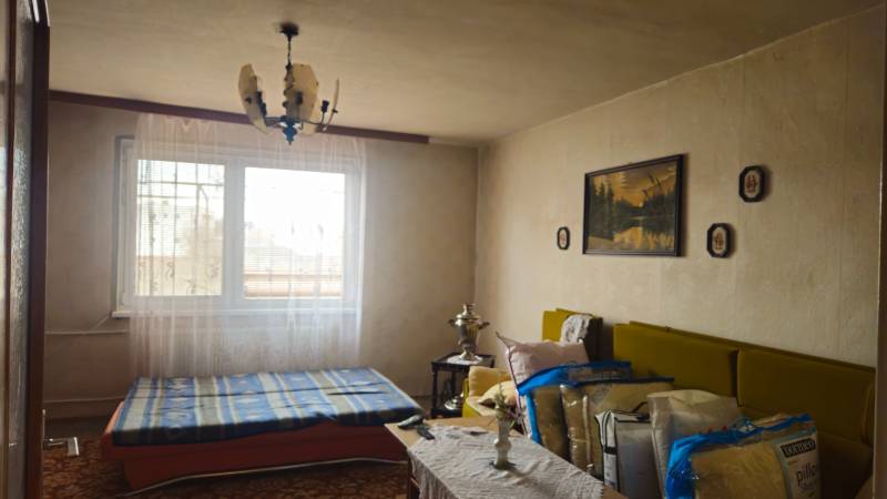 A room in a family house with a bed, a chandelier, boards, and a sofa.
