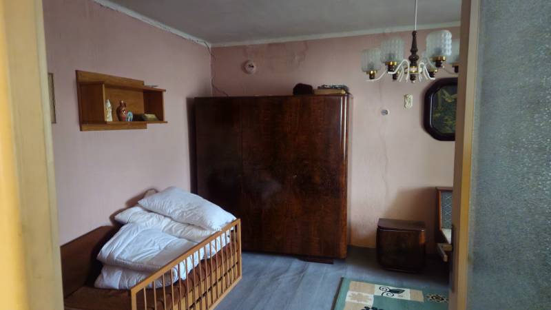 A room in a family house with a sofa, a wardrobe, a chandelier, and shelves on the walls.