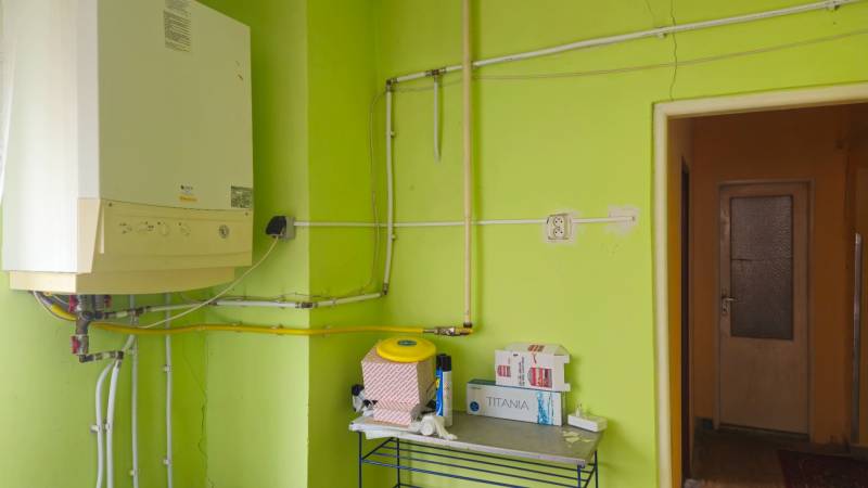 A bathroom in a family house with green walls, a boiler, and a shelf with supplies.