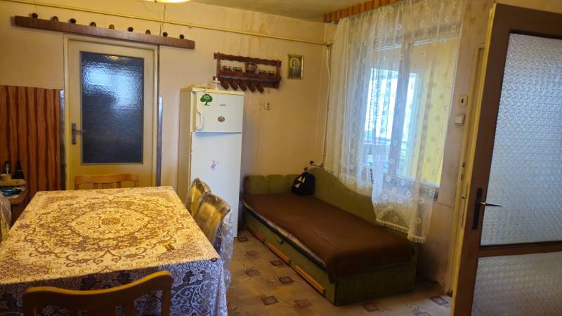 A kitchen in a family house with a tablecloth on the table, a sofa, and a refrigerator.