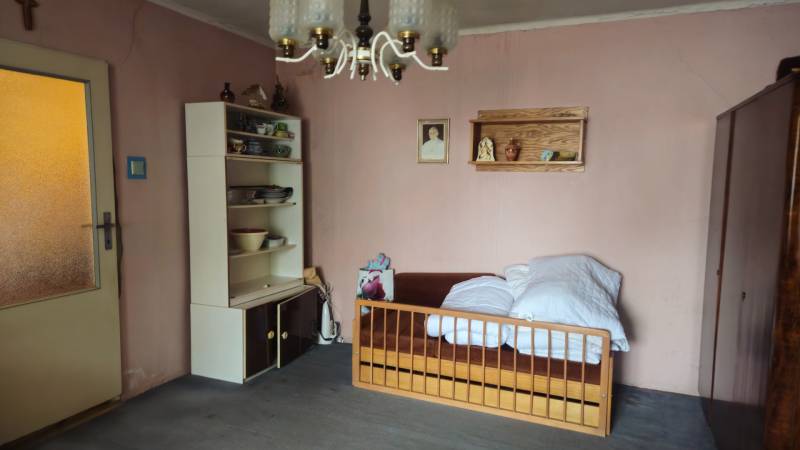 A room with a bed, shelves with dishes, and a hanging light fixture in a family house.