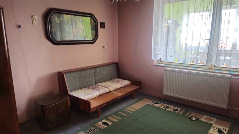 A room in a family house with a sofa, a green carpet, and an ornamental curtain.