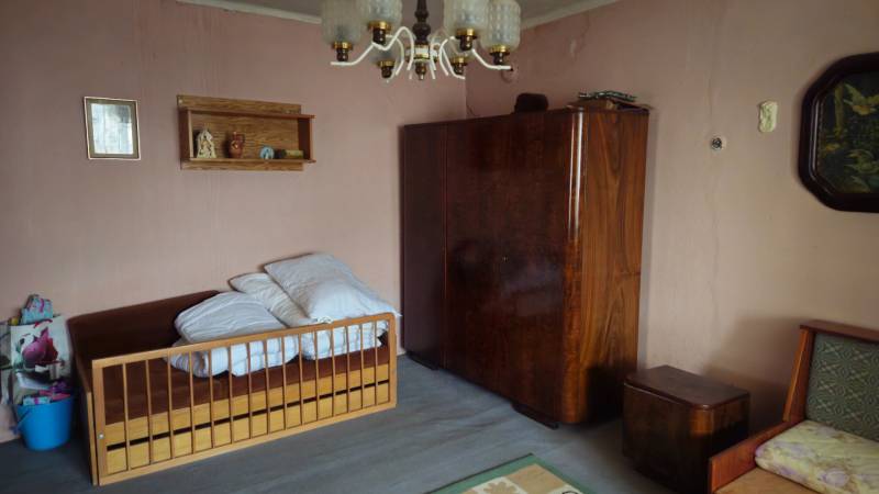 A room in a family house with a bed, a wardrobe, and a chandelier, the walls are light pink.