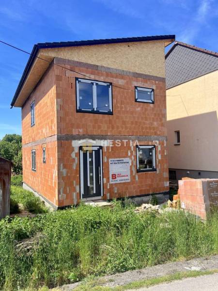 Unfinished family house in Cerová with unplastered brick walls and black window frames.