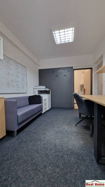 Offices with a sofa, white cabinets, a dark wall, and a floor with a wood decor.