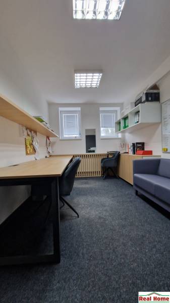 The interior of an office with desks, shelves, and chairs on a carpeted surface.