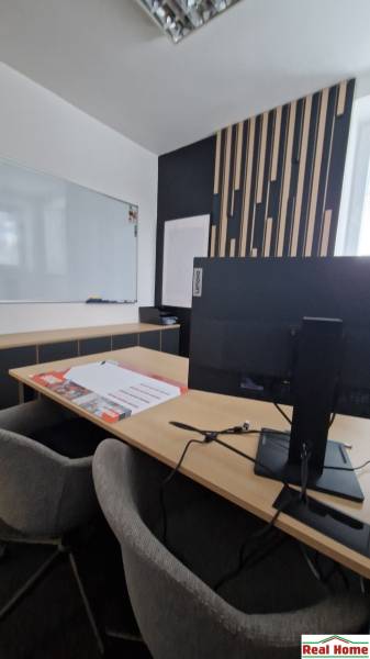 Office with a whiteboard, desk, computer, and decorative wall, equipped with comfortable chairs.