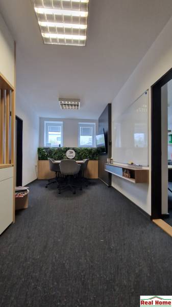 An office with a dark carpet, a whiteboard, and windows, providing a pleasant working environment.