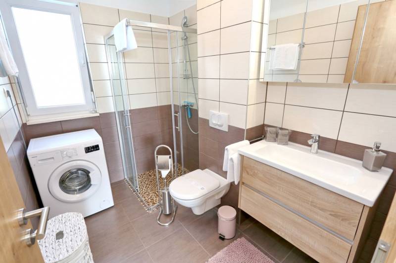 Bathroom in a 3-room apartment with a washing machine, shower, and toilet, floor with wooden decor.