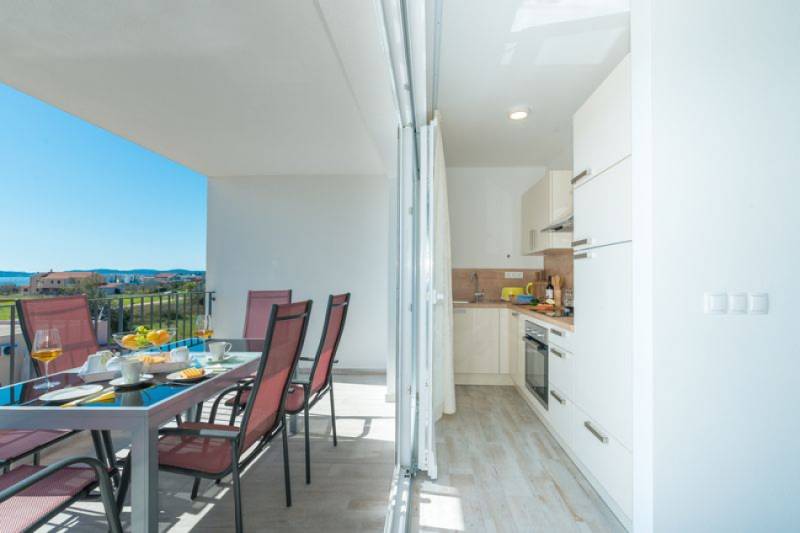 A brightly lit terrace with a dining table and a view of SUKOŠAN. Along with a kitchen.