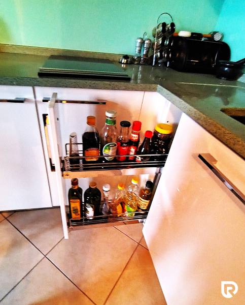 A kitchen cabinet with a pull-out organizer full of bottles and spices in a 2-room apartment.
