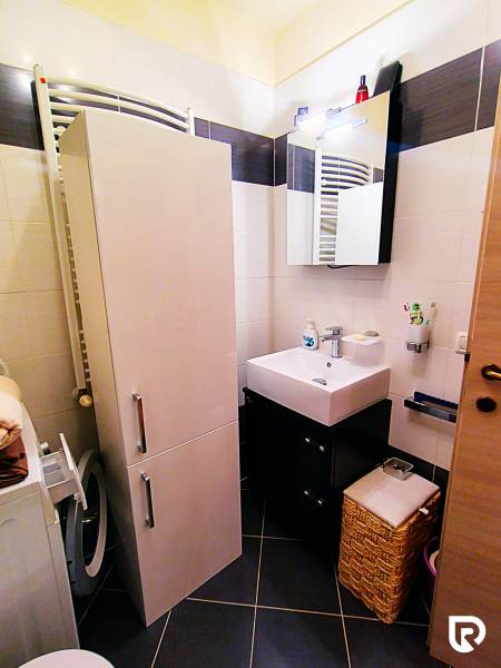 A bathroom in a 2-room apartment with a sink, storage space, and a washing machine.