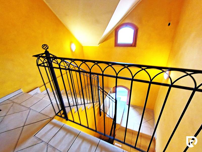 A staircase in the interior of a 2-room apartment with orange walls and wrought iron railing.