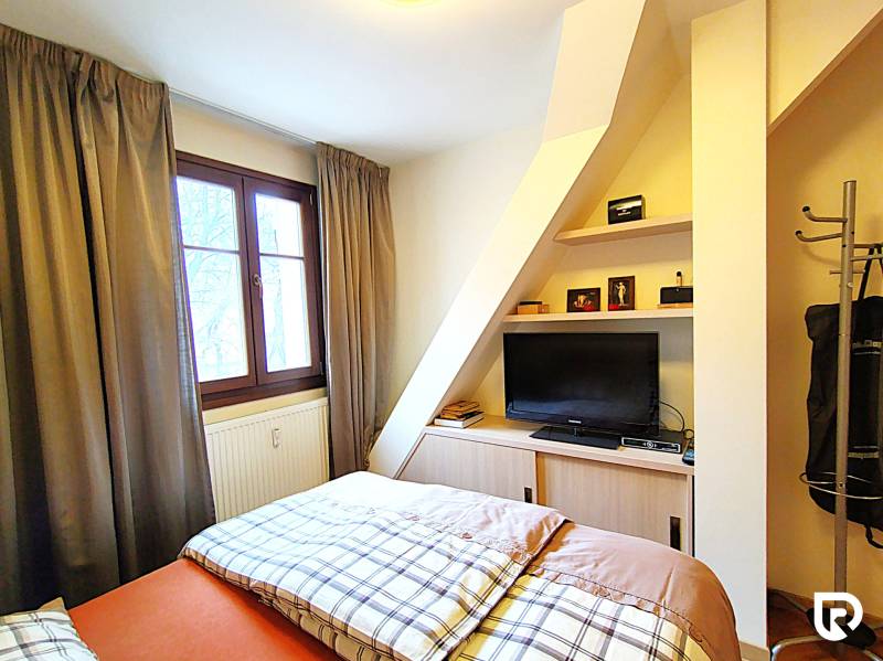 Bedroom in a 2-room apartment with a bed, television, and a window with curtains.