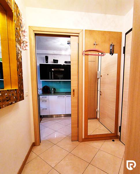 Hallway with ceramic tiles, a mirror, and an entrance to the kitchen in a 2-room apartment.