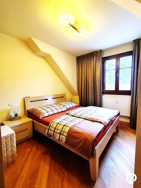Bedroom with wood-patterned flooring in a 2-room apartment, bed, nightstands, window.