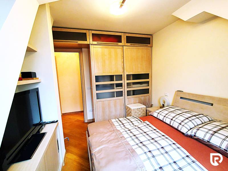 Bedroom in a two-room apartment with a wood-decor floor, a cabinet, and a television.