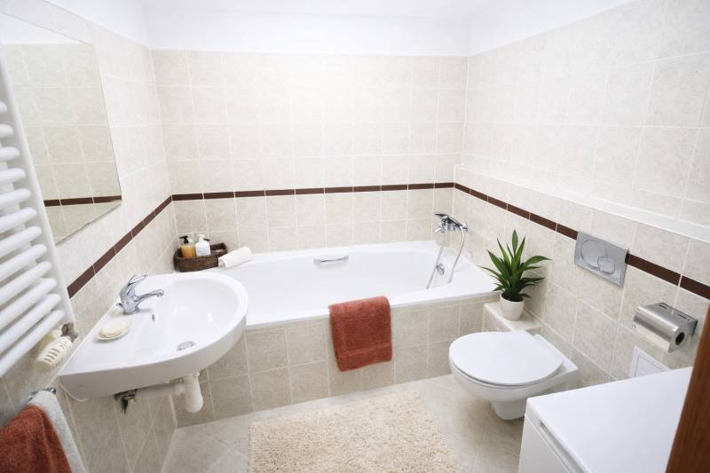A bathroom in a 2-room apartment with a bathtub and simple furnishings, cream tiles.