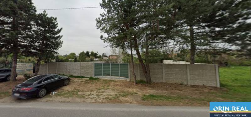 Commercial plots on Dukelská in Bernolákovo with a concrete fence and access road.