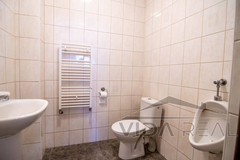 Bathroom in warehouses and halls with a toilet, urinal, and radiator on the wall.