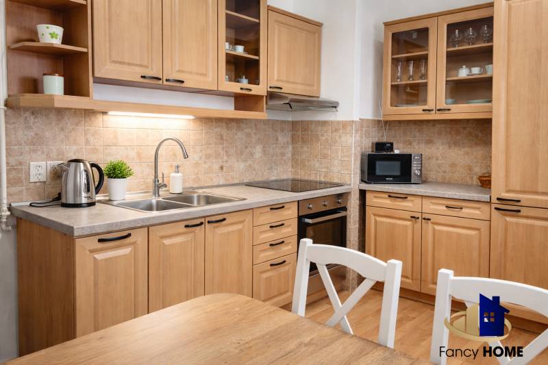 A kitchen in a 3-room apartment with wooden decor, kitchen cabinets, appliances, and a table.
