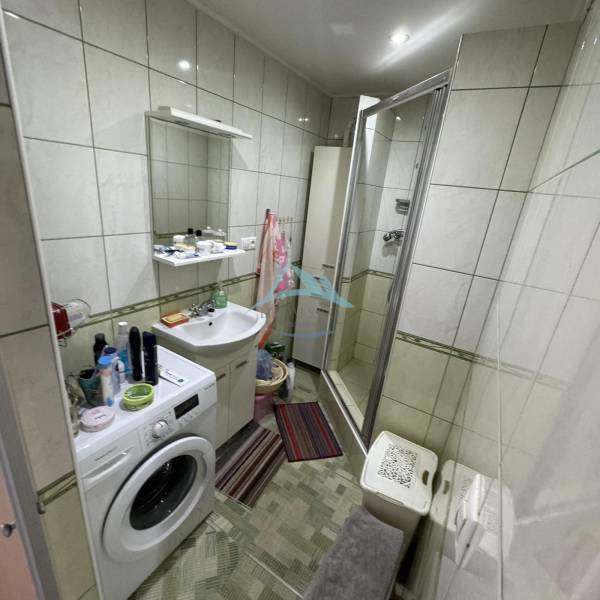 A bathroom in a 4-room apartment with a washing machine, shower corner, and tiles.