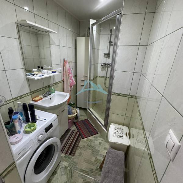Bathroom with a shower, washing machine, and sink in a 4-room apartment.