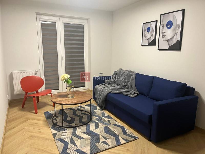 Living room in a three-room apartment with a blue sofa, a red armchair, and a wooden decor floor.
