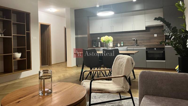 Living room in a 3-room apartment with a kitchen, table, and wooden decor flooring.