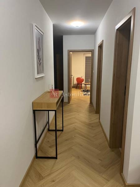 A hallway in a 3-room apartment with a wooden decor floor and furniture against the wall.