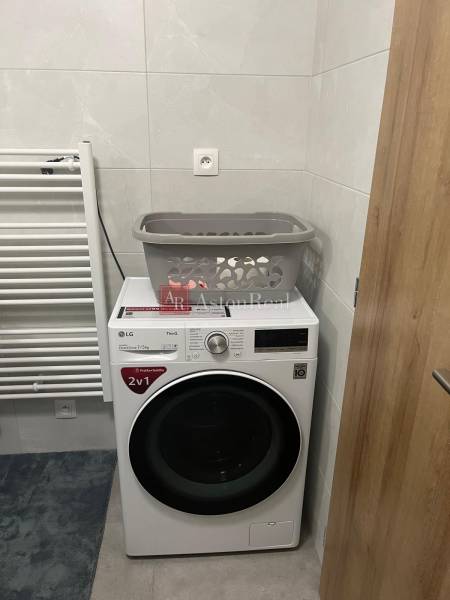 Bathroom with a washing machine in a 3-room apartment, next to a radiator on white tiles.