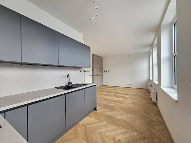 A kitchen in a studio apartment with a wood-patterned floor and large windows.