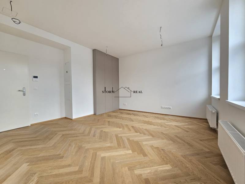 A spacious room in a one-bedroom apartment with a wooden decor floor and large windows.