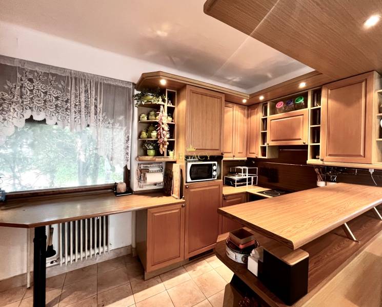 A kitchen in a family house with wooden cabinets and decor, tiled floor, flowers on the shelf.