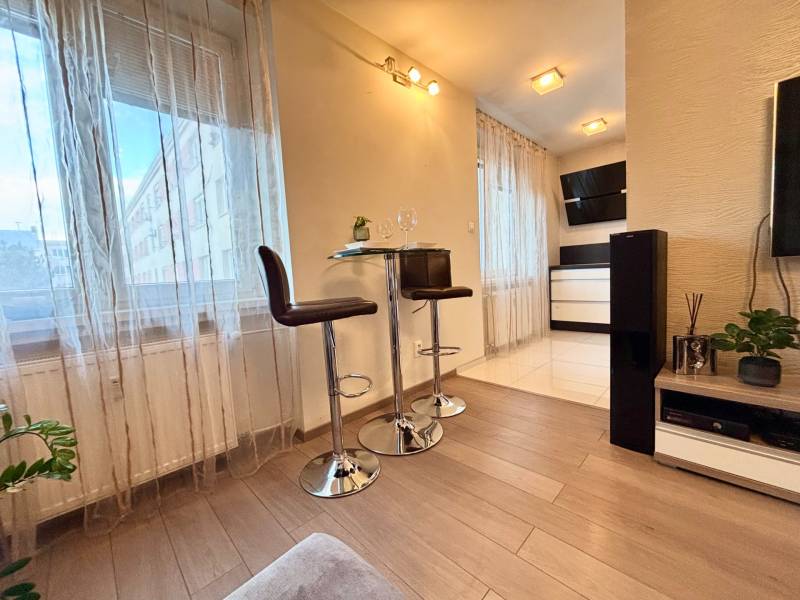 Interior of a 2-room apartment with a wooden decor floor, bar stools, and decorations.