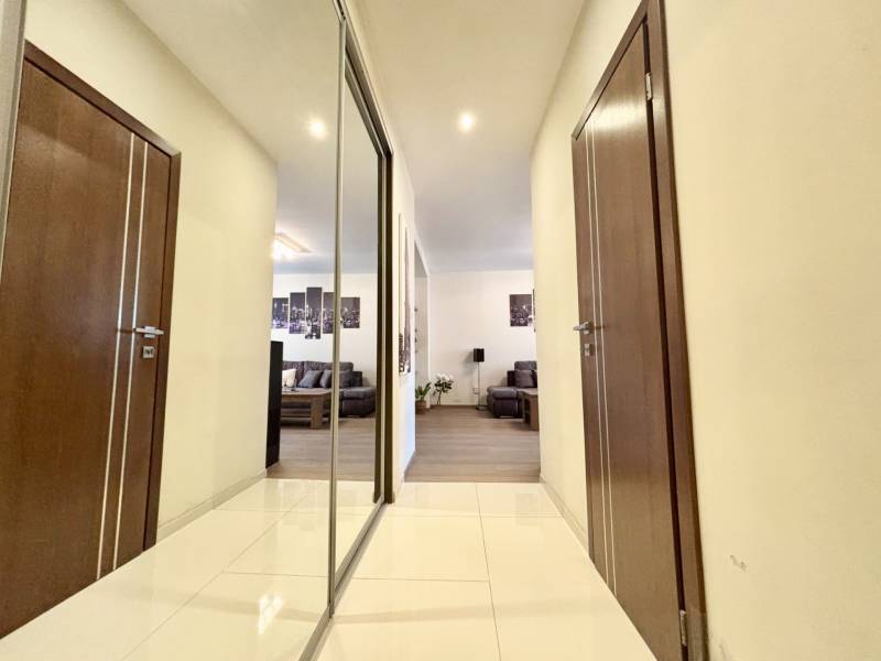 A hallway in a 2-room apartment with tiles, a mirror, and a view into the living room.